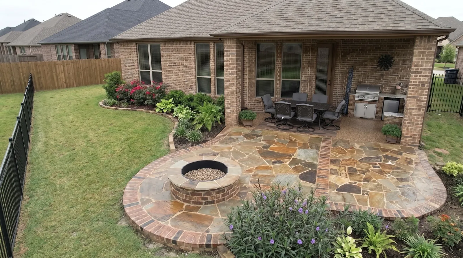Custom flagstone patio with brick-bordered fire pit and covered outdoor kitchen built by Parker County Masonry