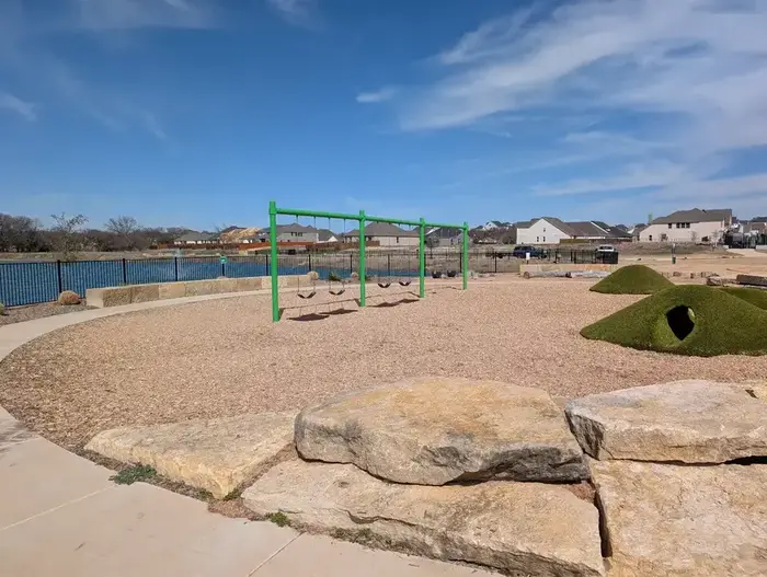 Commercial swing set with natural boulder edging and turf hill tunnel on wood fiber surfacing